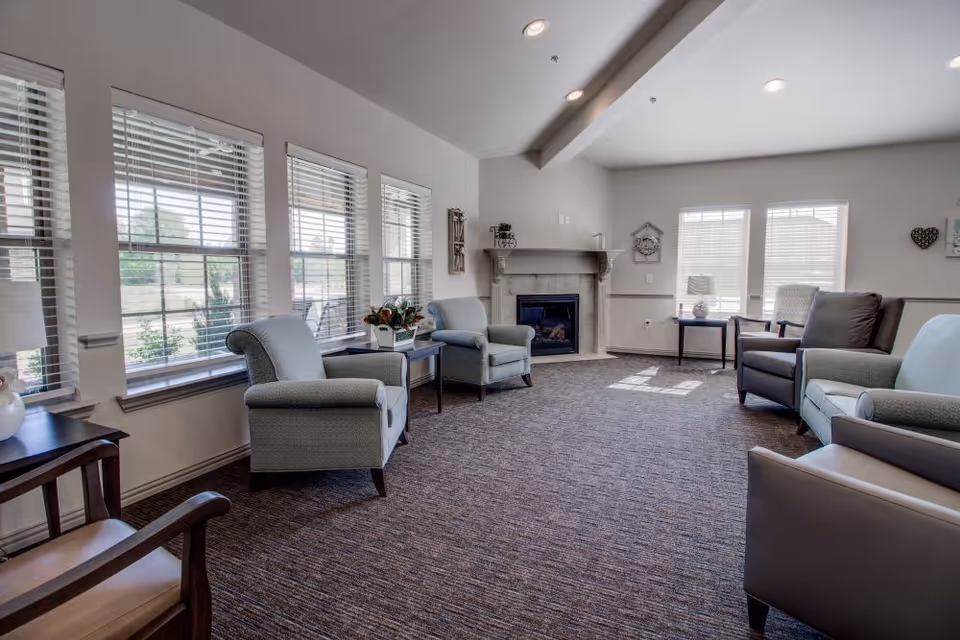 Bright common living room with multiple armchairs arranged around a fireplace and large windows.