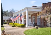 Front exterior of Merry Wood Lodge featuring American flags, brick facade, and rocking chairs.