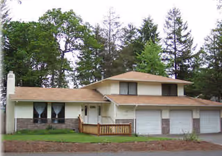 A residential building with a three-bay garage and surrounding trees in a suburban setting.