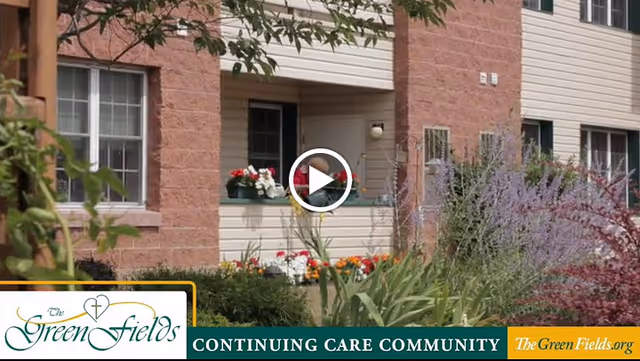 Front exterior of The GreenFields continuing care building with flower beds and a covered entryway.