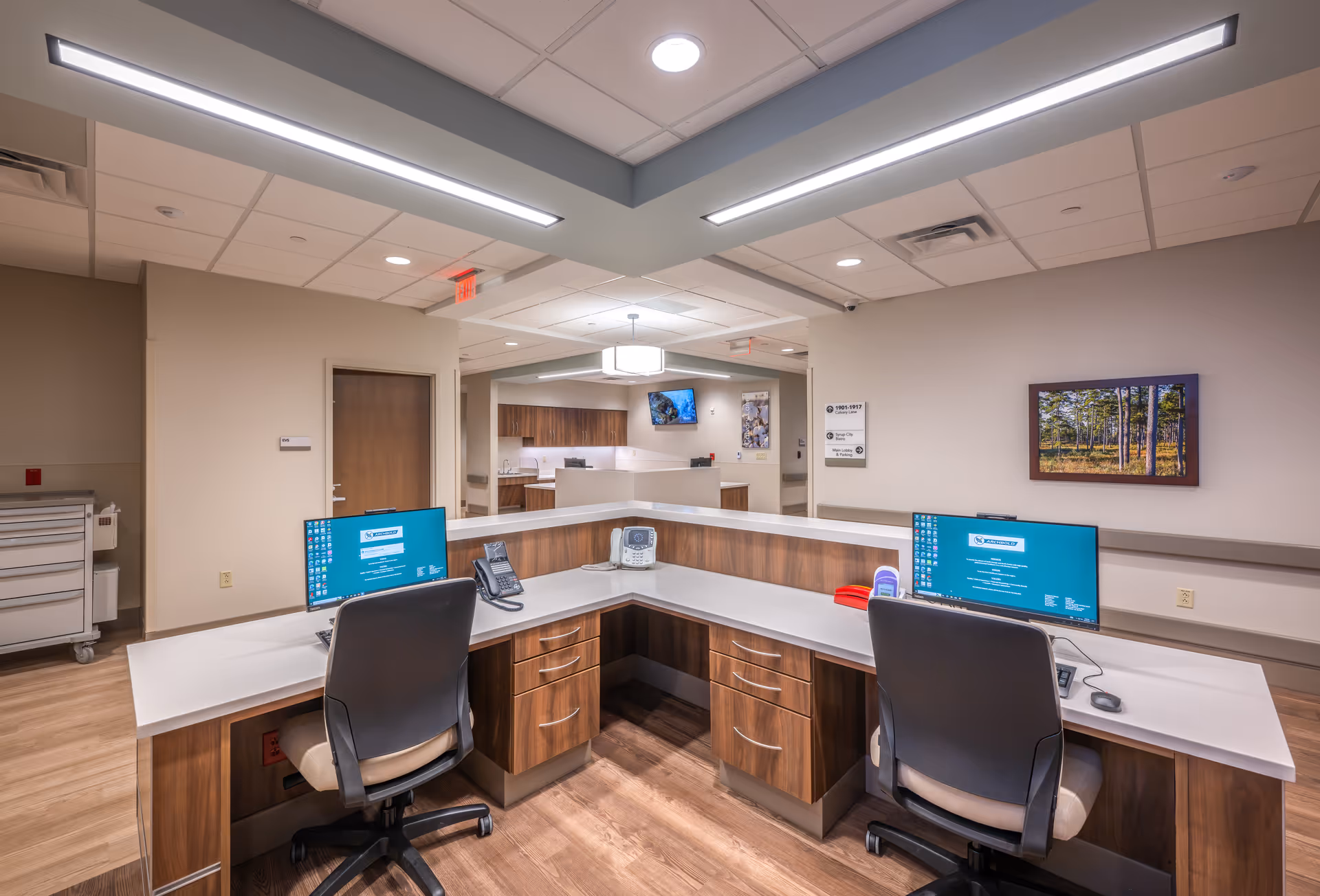 Well-lit interior reception/nurse station with a U-shaped desk, two computer monitors, office chairs, and wood cabinetry.