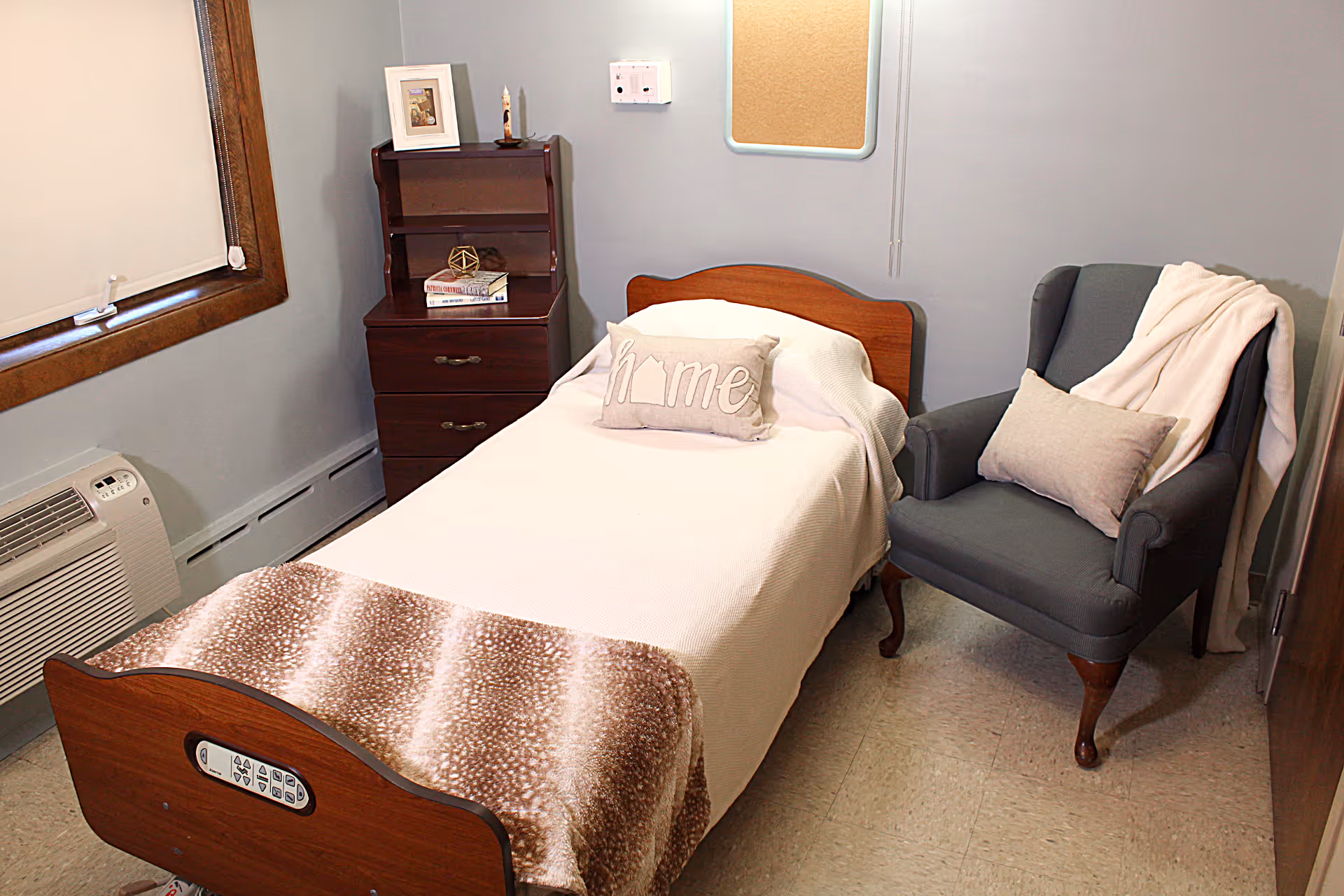 A small bedroom with a single bed, wooden nightstand, upholstered armchair and a window.