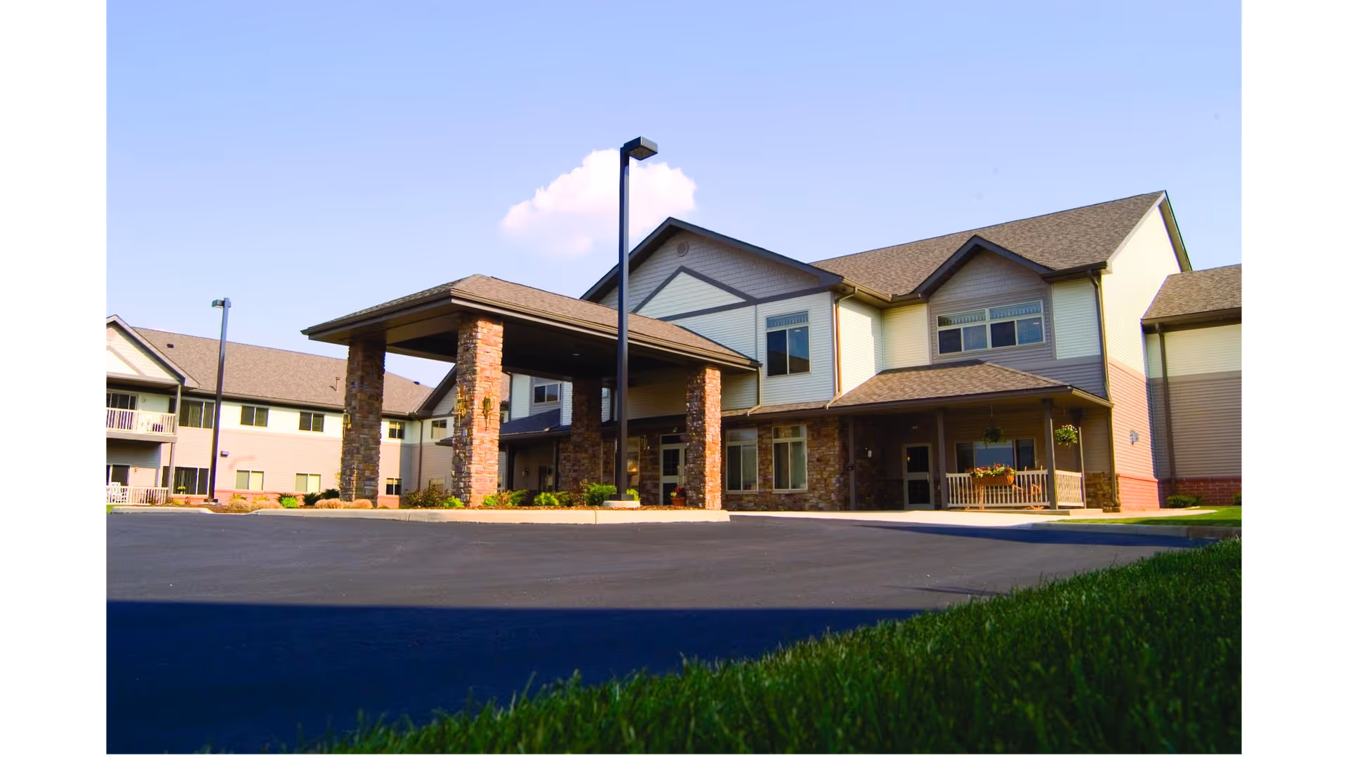 Front exterior of a two-story retirement community building with a covered entrance and parking area.