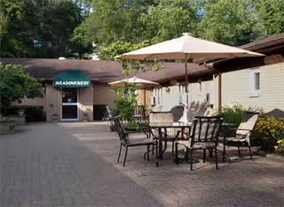 Outdoor courtyard with patio tables, chairs, and umbrellas beside Meadow Crest Rehabilitation and Healthcare Center.