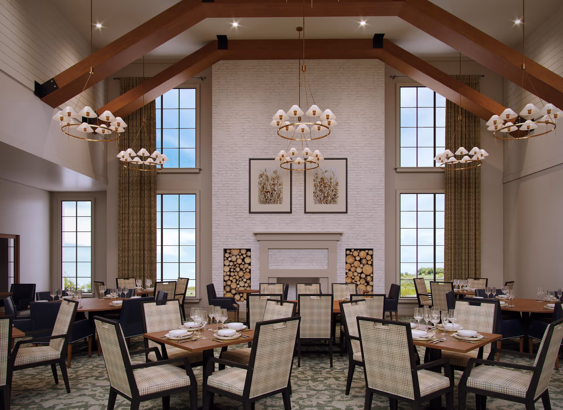 A spacious dining room with multiple wooden tables set with plates, glasses, and silverware. The room features high ceilings with exposed wooden beams, large windows with curtains, and a white brick fireplace with stacked firewood on either side. Elegant chandeliers hang from the ceiling, illuminating the room.