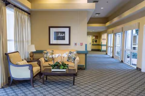 Bright senior living facility lobby lounge with beige seating and large windows.