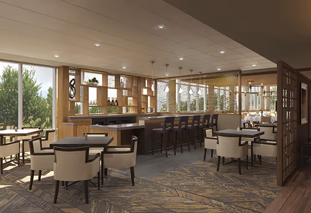 Spacious dining room with multiple tables and chairs surrounding a central bar area and large windows showing greenery outside.