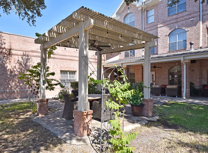 Outdoor courtyard featuring a pergola with seating and wicker chairs in front of a brick building.