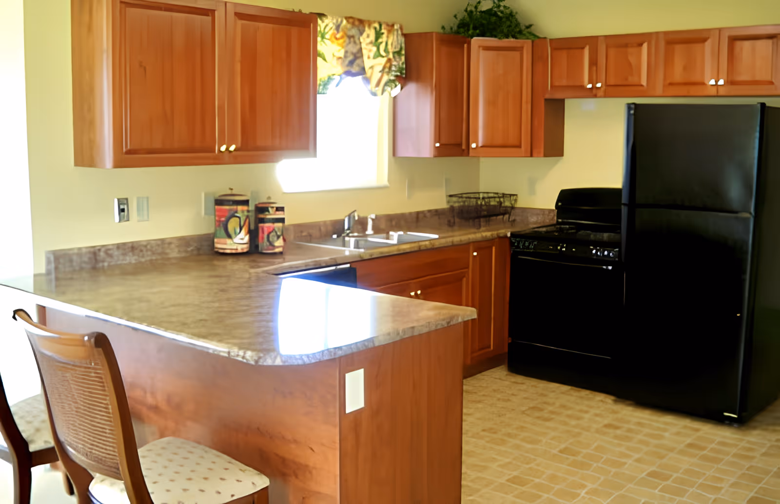 Bright kitchen with wooden cabinets, a black refrigerator and stove, and a countertop island with seating.
