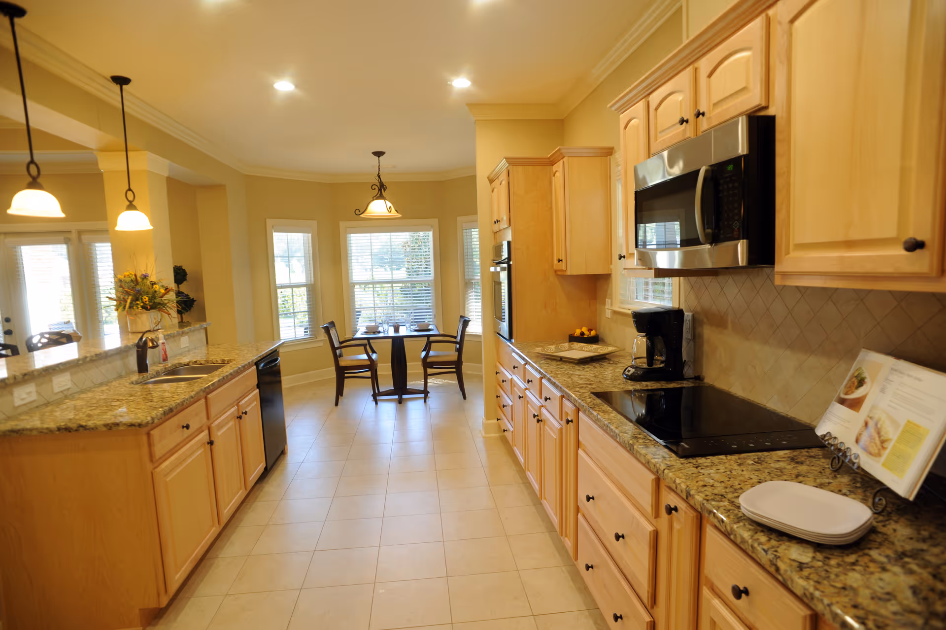 Spacious kitchen with granite countertops, light wood cabinets, stainless microwave, and a breakfast nook with a round table by bay windows.