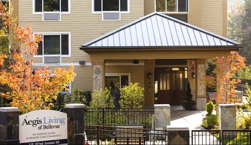Exterior front entrance of Aegis Living of Bellevue, an assisted living and memory care community, showing a covered entryway, windows, and landscaped garden with autumn-colored trees.