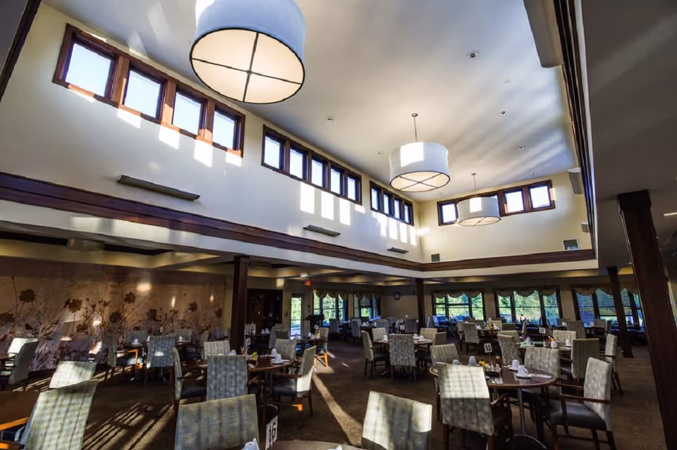 Spacious dining room with multiple tables and chairs beneath high ceilings and large pendant lights.