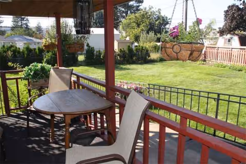 Outdoor porch with round table and chairs overlooking a green backyard.