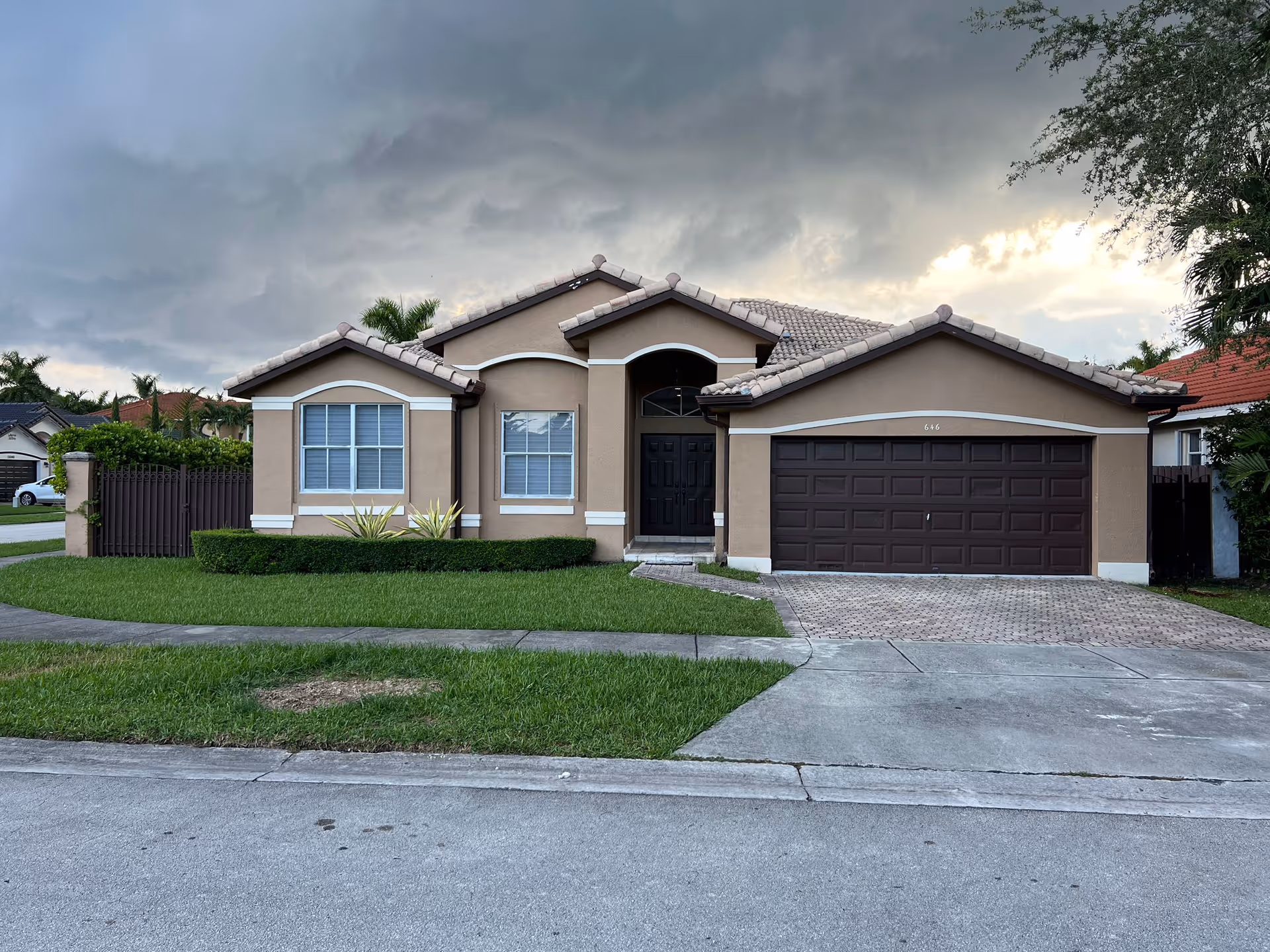 Single-story beige stucco house with a two-car garage and front lawn under a cloudy sky.