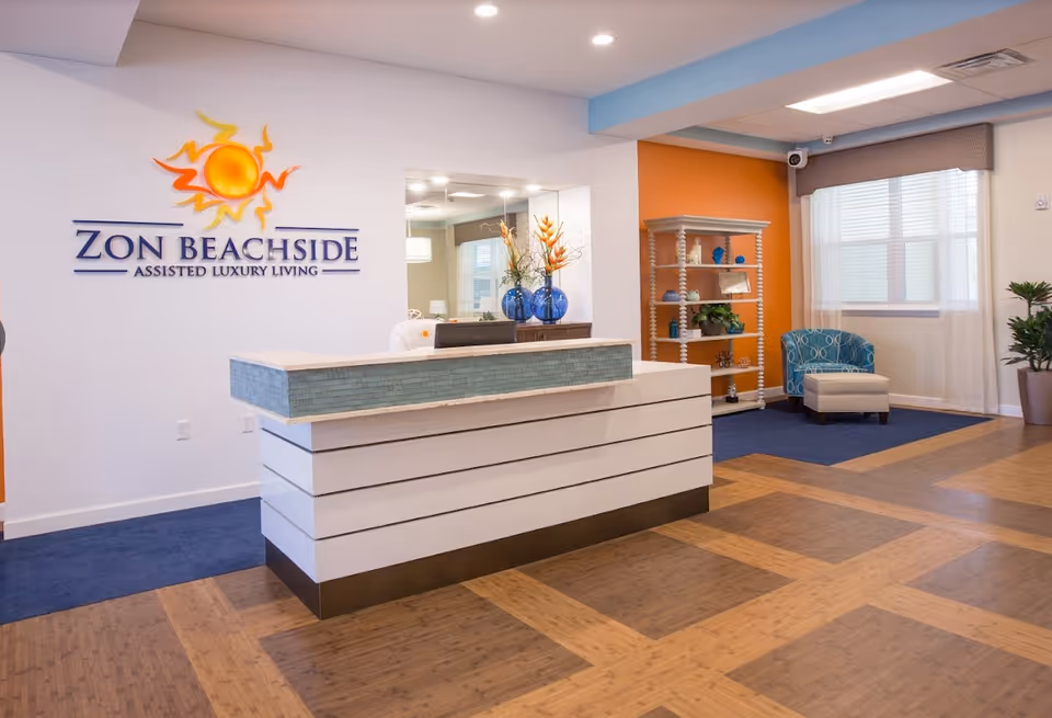 Reception desk and bright lobby of Zon Beachside with the facility logo on the wall, seating, and decorative shelving.