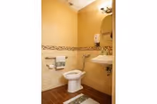 Accessible bathroom with a toilet, wall-mounted sink, round mirror, grab bars, and tiled walls and floor.