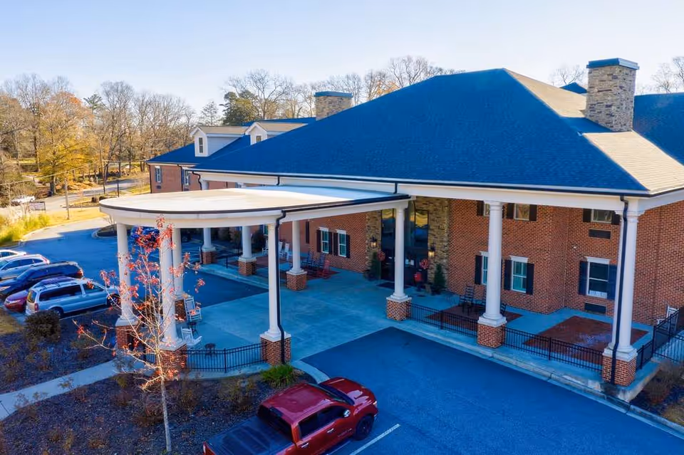 Front entrance of a brick senior living building with a covered porte-cochère supported by white columns and a parking area.
