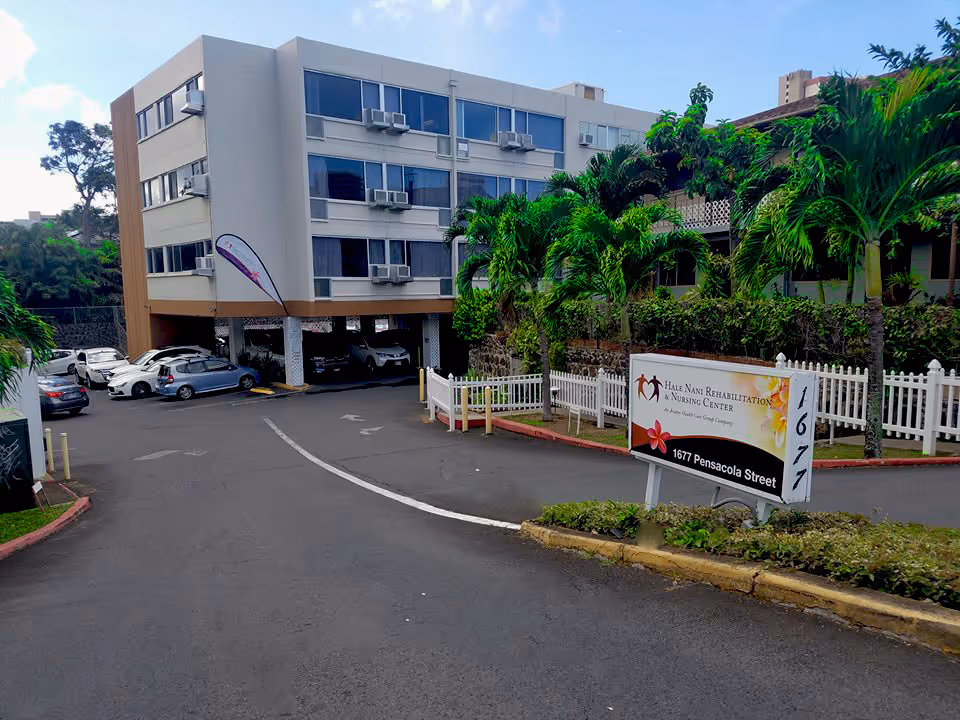 Driveway and entrance sign for Hale Nani Rehabilitation & Nursing Center beside a multi-story building with palm trees and parked cars.