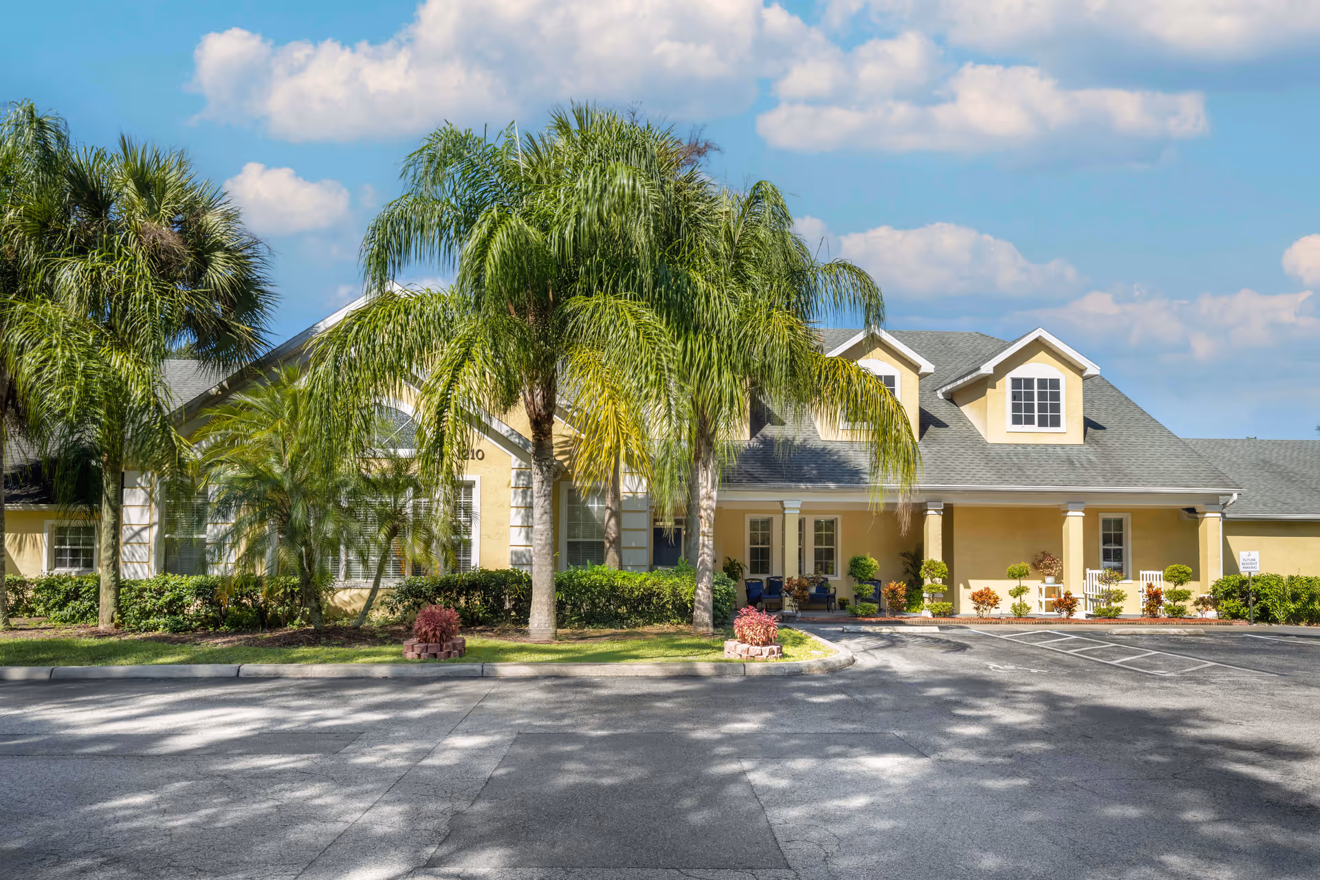 Sunny senior living facility with a beige building, palm trees, and a welcoming entrance.