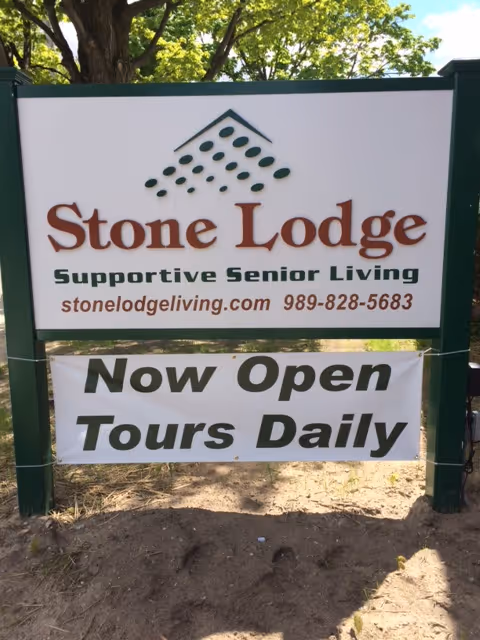 Outdoor sign for Stone Lodge Supportive Senior Living with a 'Now Open Tours Daily' banner.