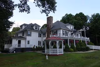 Two-story white manor with a red-roof gazebo and manicured lawn.