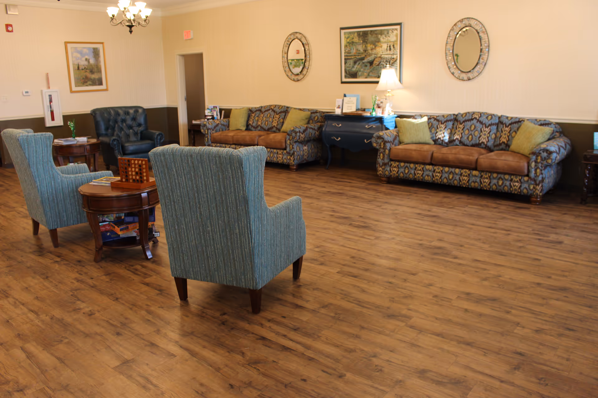 Spacious senior living room with patterned sofas, upholstered armchairs, side tables and wood-look flooring.