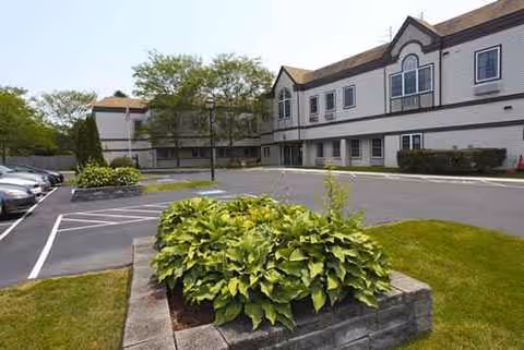 Exterior view of Village House Nursing and Rehabilitation Center with parking lot.