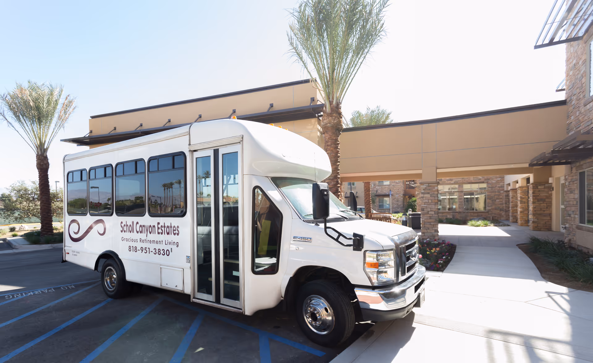 A white shuttle bus parked in front of Scholl Canyon Estates retirement living facility.