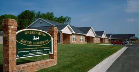 Exterior view of Warrensburg Senior Apartments with green sign and brick buildings.