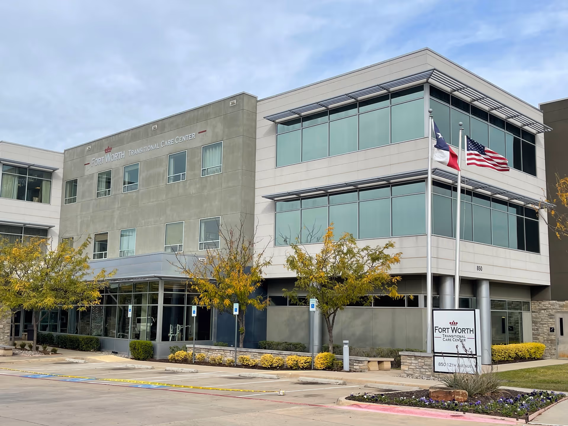 Front exterior of the Fort Worth Transitional Care Center building with flags flying and a landscaped entrance.
