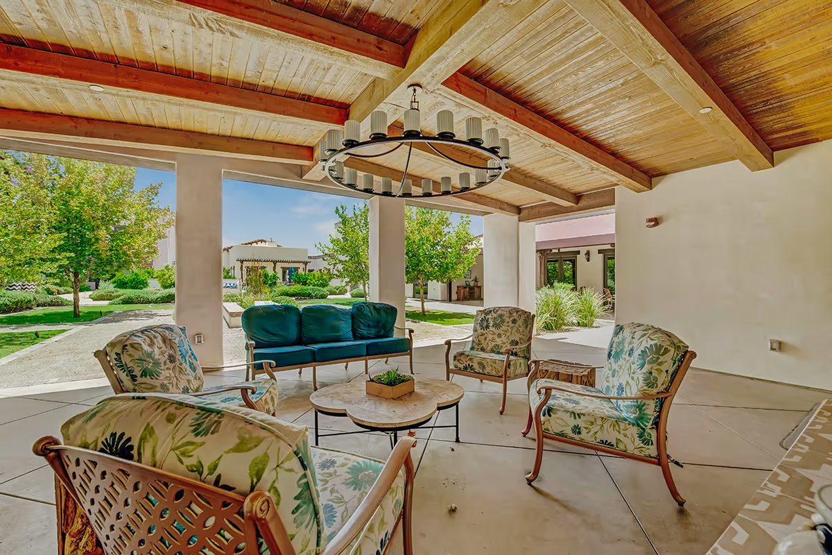 Covered outdoor patio with cushioned chairs and a sofa arranged around a coffee table overlooking landscaped grounds.