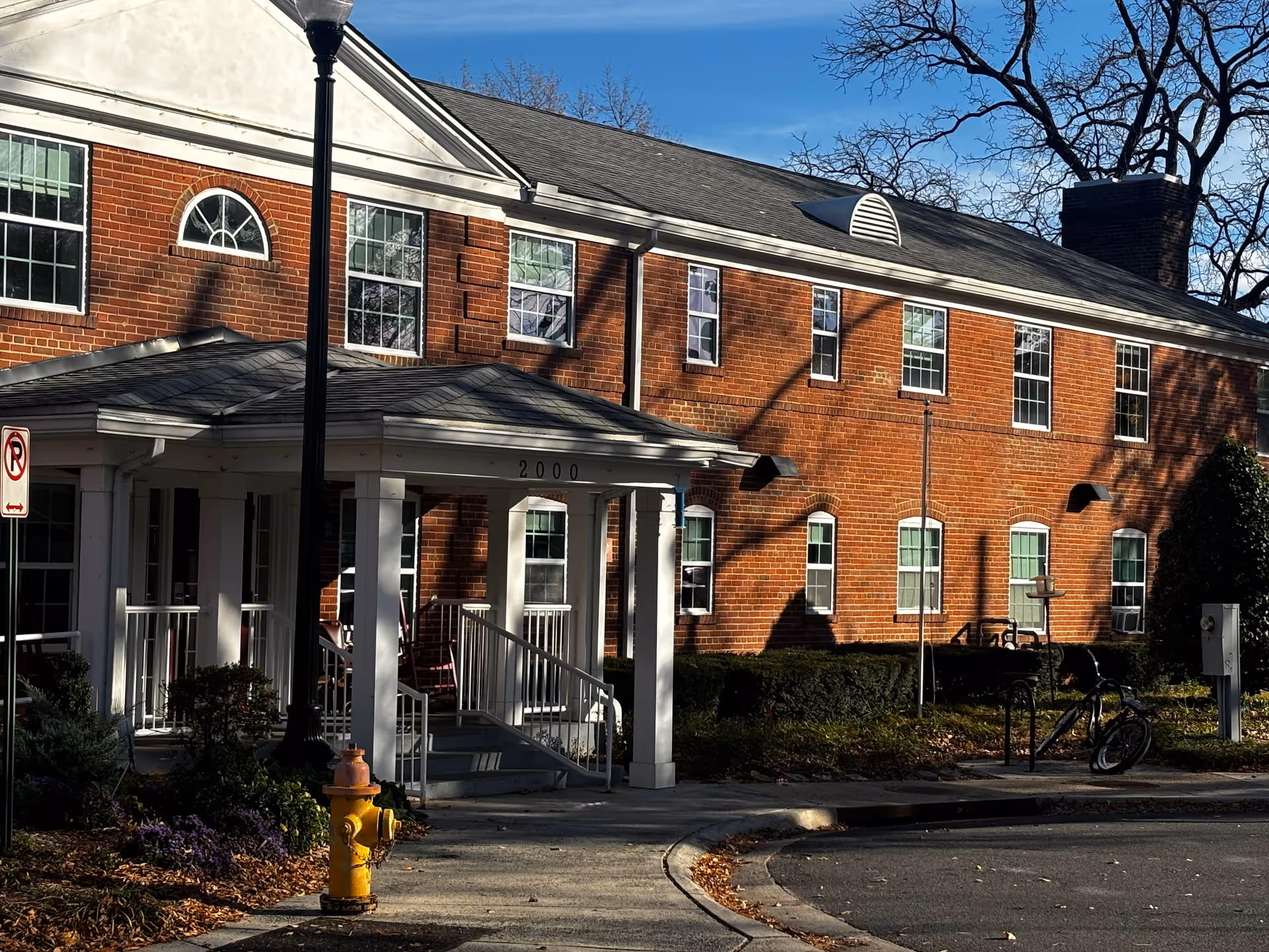 Two-story red brick assisted living building with a white columned entrance canopy (2000) and a yellow fire hydrant in front.