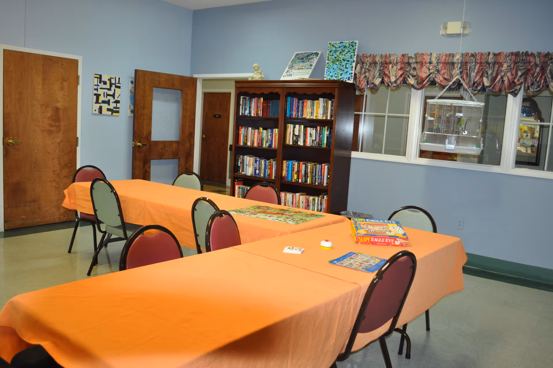 Activity/common room with orange-covered tables and chairs, a bookshelf, and board games.