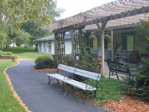 Exterior view of Plum City Care Center with a bench, pergola, and landscaped walkway.