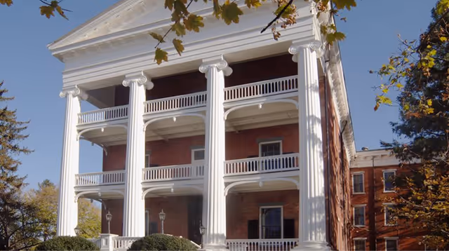Front facade of a three-story brick building with large white classical columns and covered balconies.