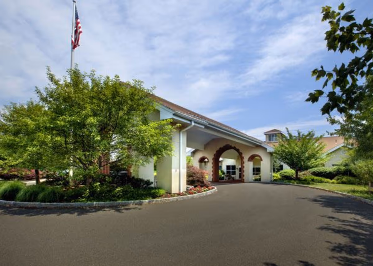 Front entrance and covered porte-cochère of Brittany Pointe Estates with a driveway, landscaping, and an American flag.