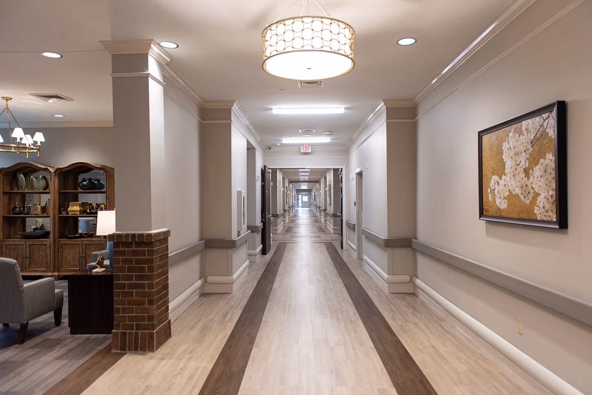 Long, well-lit interior hallway of a senior living facility with a seating area on the left and artwork on the right.
