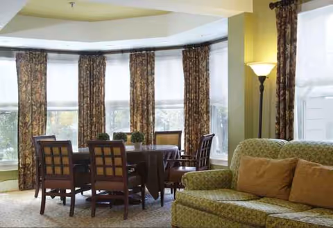 Sunlit interior dining area with a round table, chairs, sofa, and floor lamp.