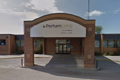 Brick building front with a curved white sign Perham Living over the glass entrance.