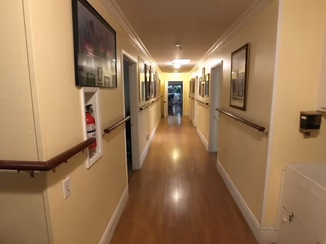 Long, well-lit interior corridor with wooden floors, handrails, and framed pictures along the walls.