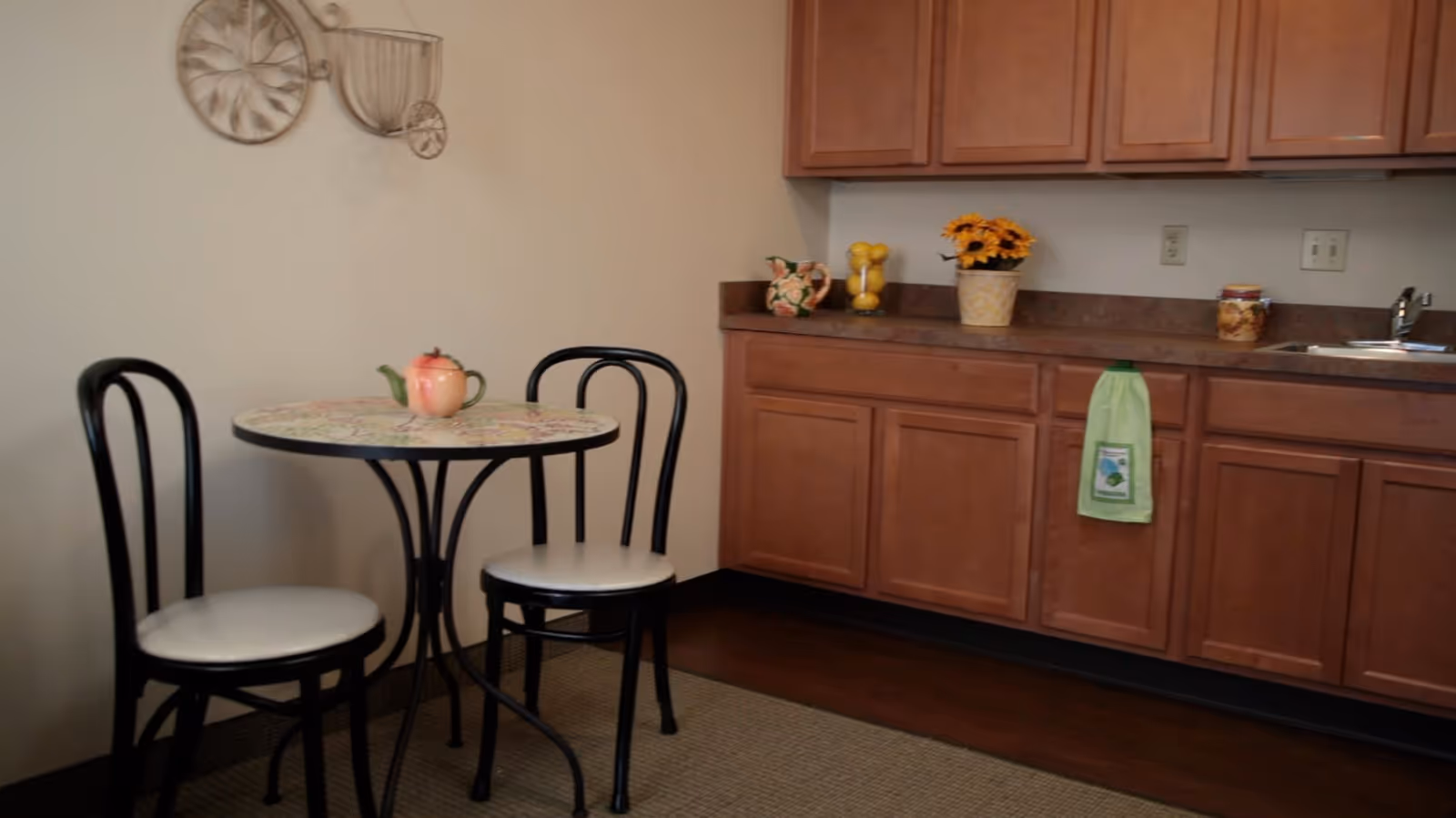 Small kitchenette with wooden cabinets, a sink and a round bistro table with two chairs.