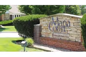 Stone and brick sign at the entrance of a facility with the text 'Maria Court' and 'A Ministry of the Sisters of St. Joseph', surrounded by greenery and a paved driveway.