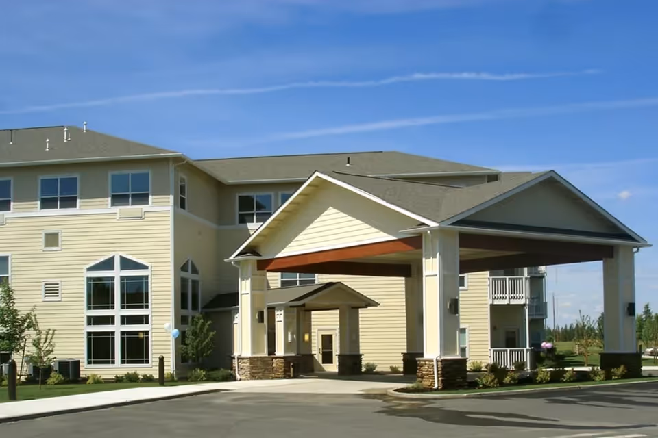Entrance and covered porte-cochère of a multi-story senior living building under a blue sky.