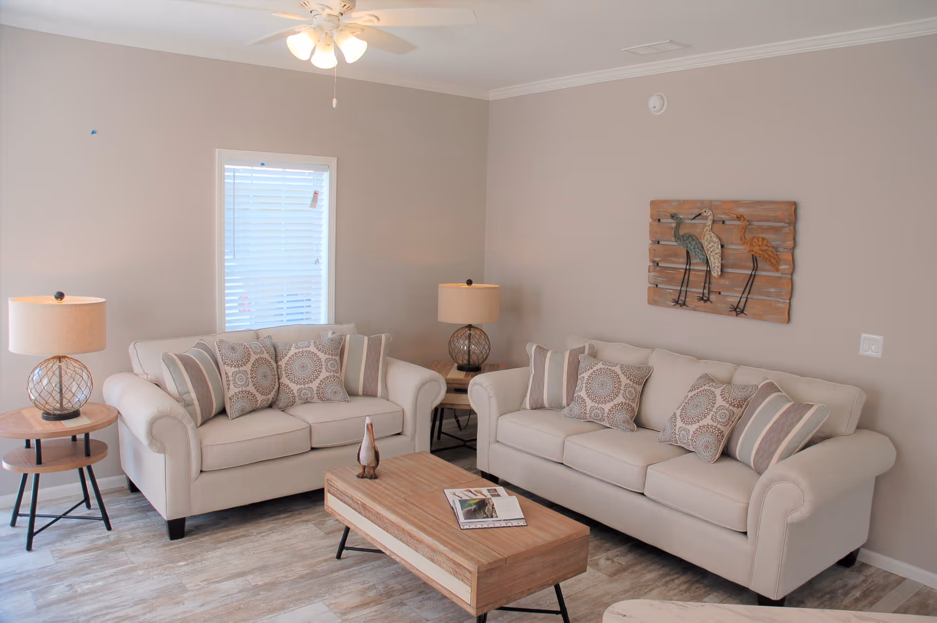 Living room with two beige sofas, a wooden coffee table, matching lamps, and bird wall art on a neutral wall.