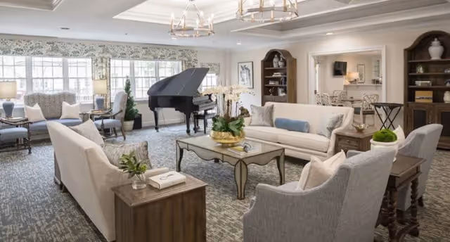Elegant senior living lounge with sofas, armchairs, a coffee table, and a grand piano by large windows.