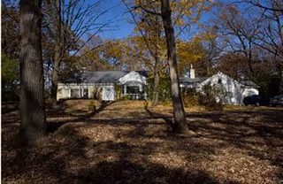 Exterior view of a white senior living home surrounded by trees and fallen autumn leaves.