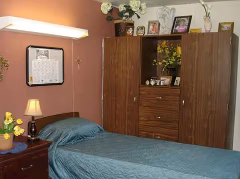 A small bedroom with a single bed, nightstand, lamp, and large wooden wardrobe.