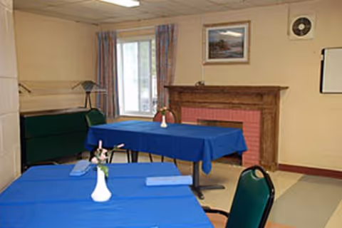 Interior dining room with blue tablecloths, green chairs, a white vase, and a fireplace.