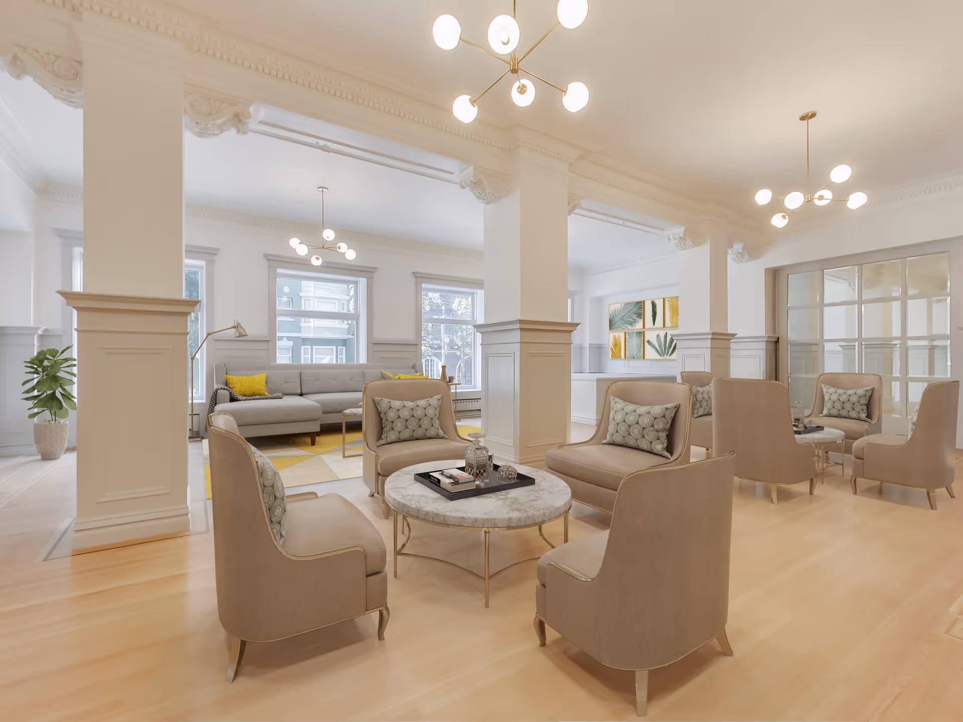 A spacious and elegant living room area with beige armchairs arranged around round marble coffee tables. There is a large gray sectional sofa with yellow accent pillows near the windows. The room features white walls, large windows, decorative columns, and modern ceiling light fixtures. A potted plant and framed artwork with leaf designs add a touch of greenery to the space.