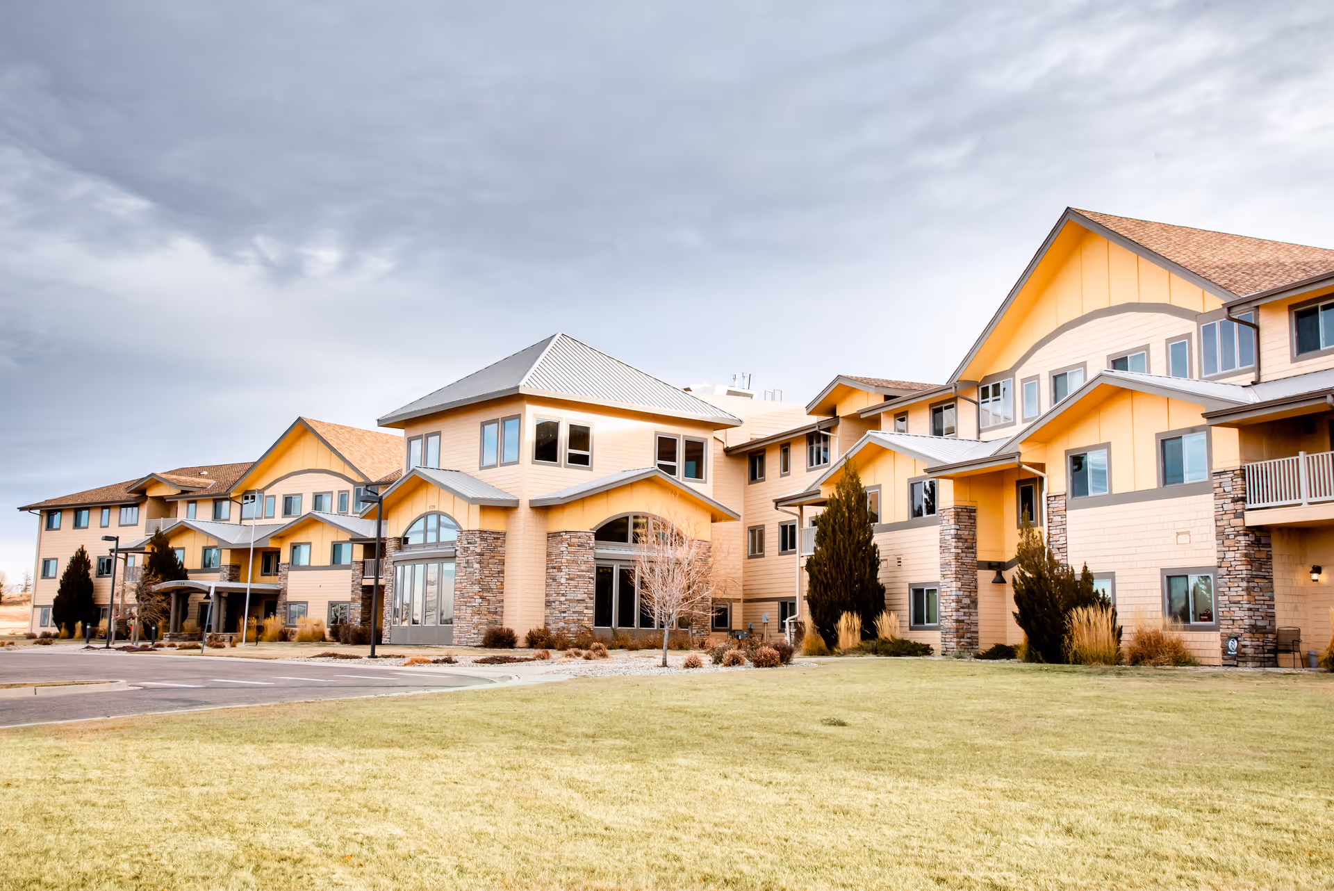Front exterior of a multi-story yellow senior living facility with a lawn and cloudy sky.